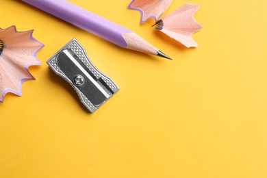 Photo of Pencil, sharpener and shavings on yellow background, flat lay. Space for text