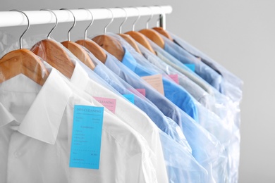 Photo of Rack with clean clothes on hangers after dry-cleaning against light background