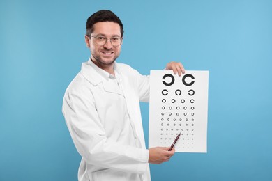 Photo of Ophthalmologist pointing at vision test chart on light blue background