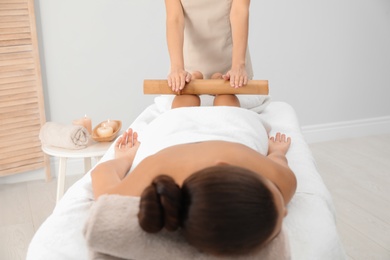 Photo of Young woman having massage with bamboo stick in wellness center