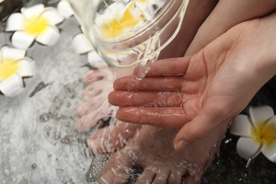 Woman pouring water onto hand while soaking her feet in bowl, above view. Spa treatment