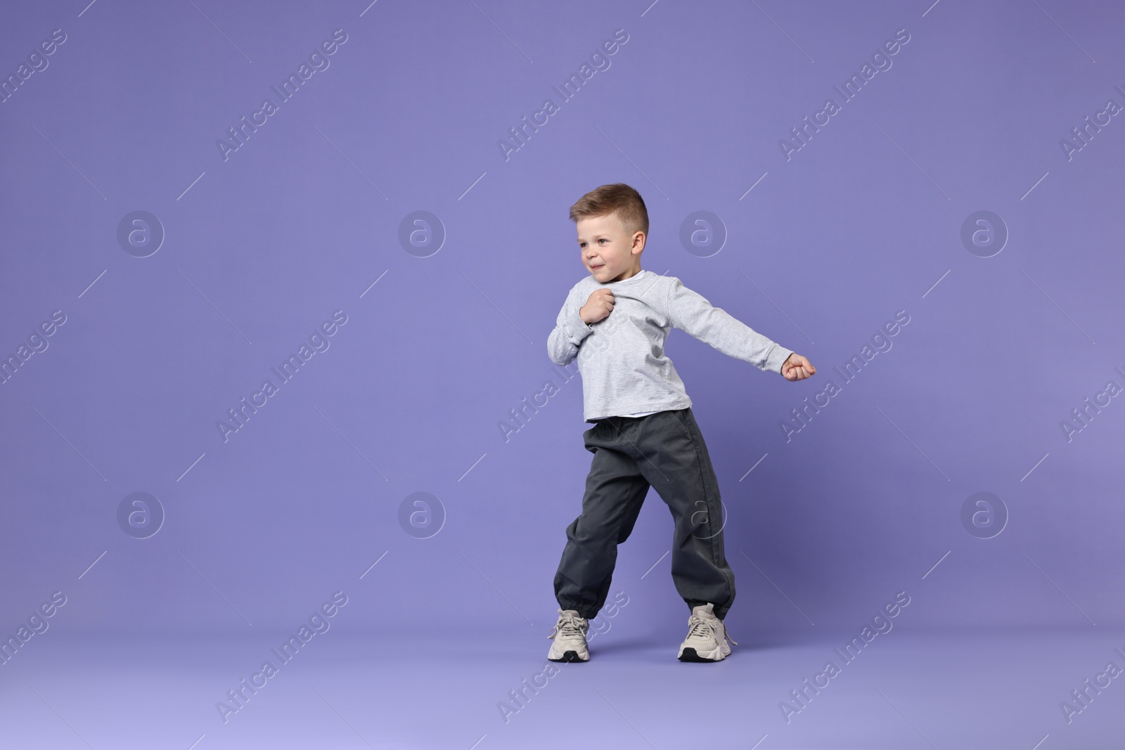 Photo of Happy little boy dancing on violet background. Space for text