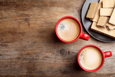 Breakfast with delicious wafers and coffee on wooden table, flat lay. Space for text