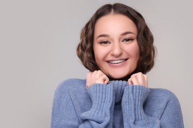 Smiling woman with dental braces in warm sweater on grey background. Space for text