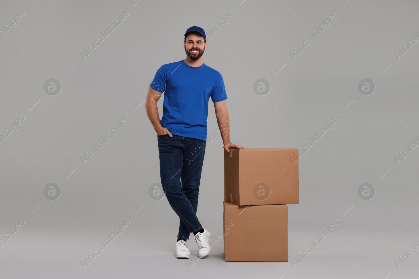 Photo of Happy young courier with parcels on grey background