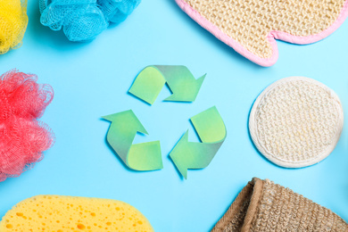 Photo of Recycling symbol, plastic and natural shower sponges on light blue background, flat lay