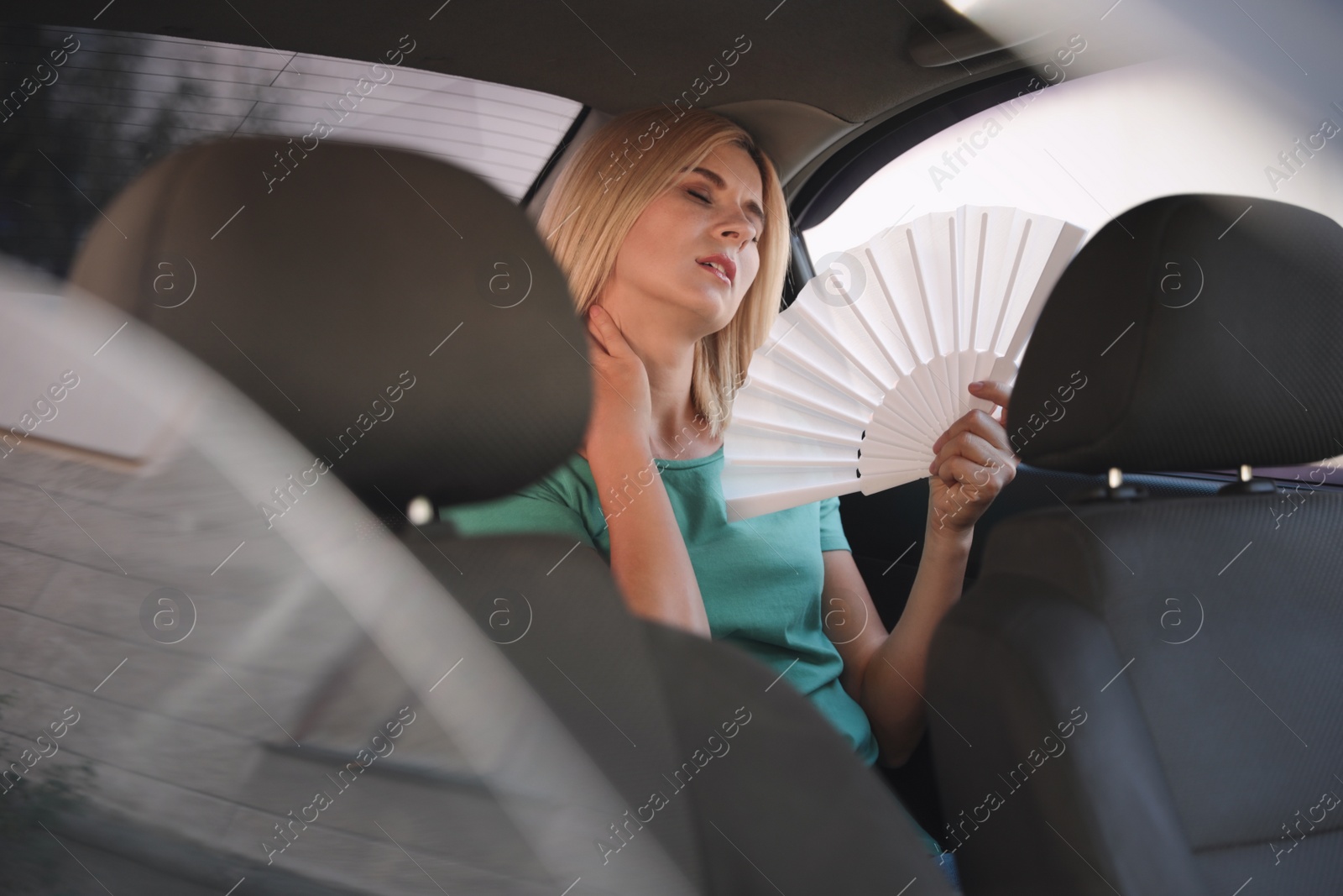 Photo of Woman with hand fan suffering from heat in car. Summer season