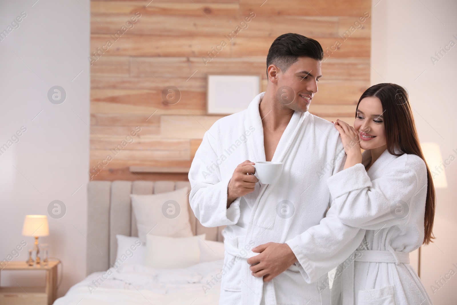 Photo of Happy couple in bathrobes with coffee in bedroom