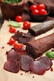 Delicious dry-cured beef basturma with basil, tomatoes and spices on table, closeup