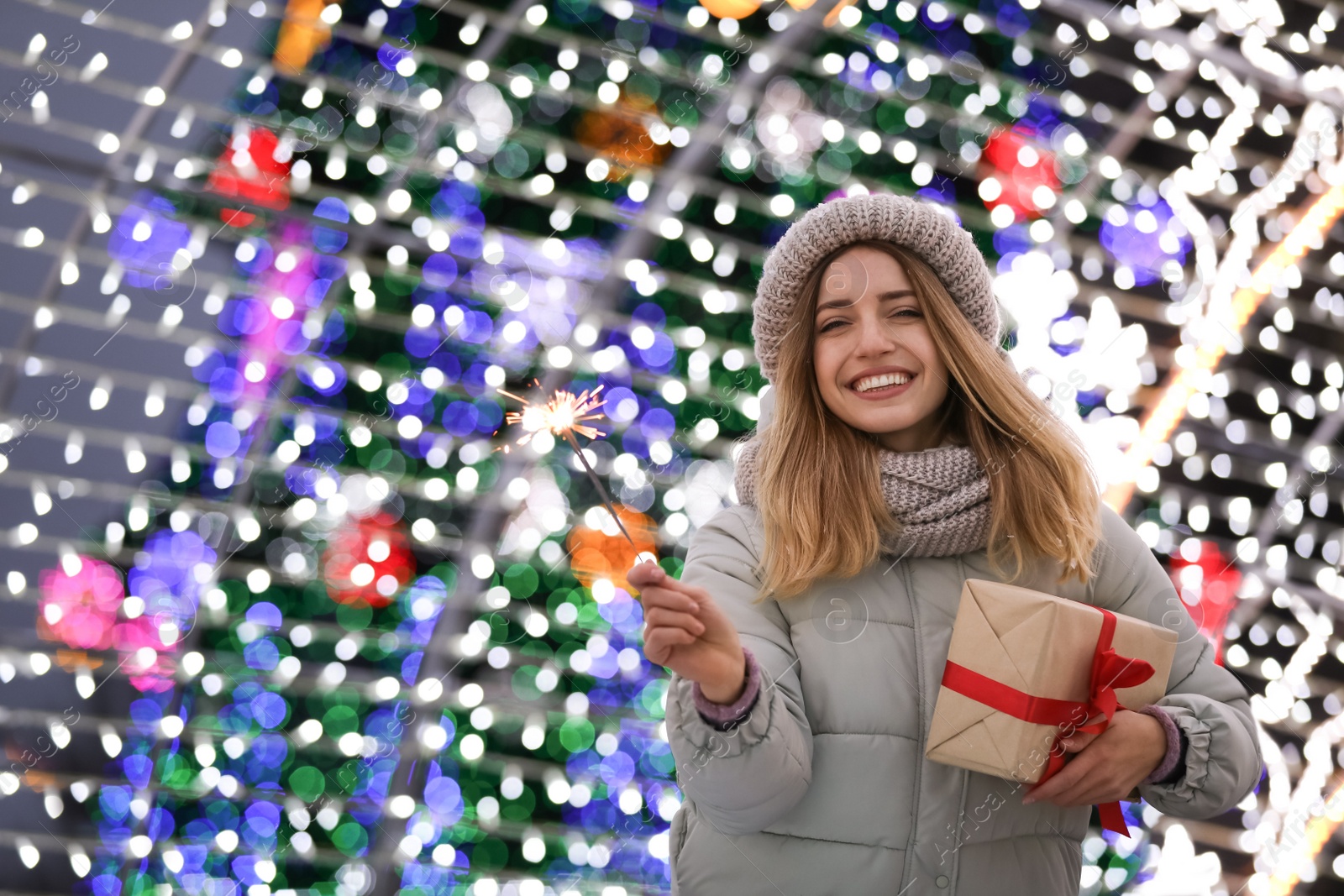 Photo of Happy young woman with gift box near festive lights. Christmas celebration