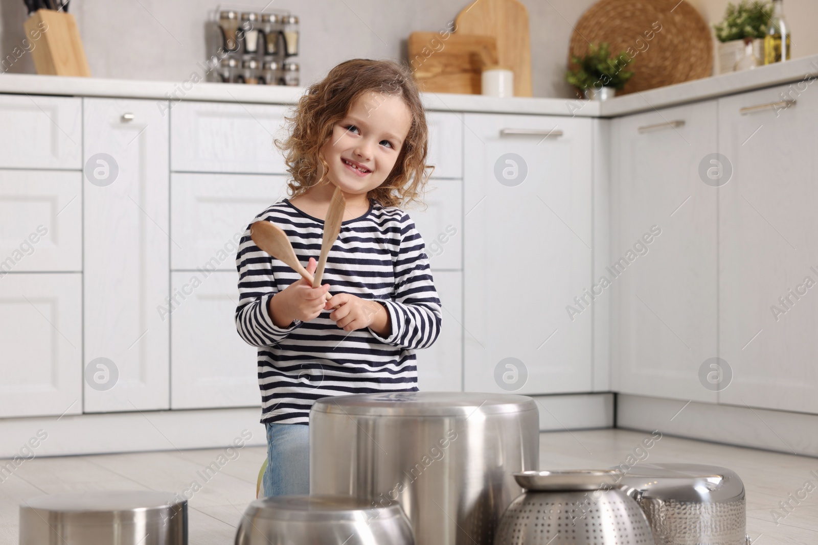 Photo of Little girl pretending to play drums on pots in kitchen