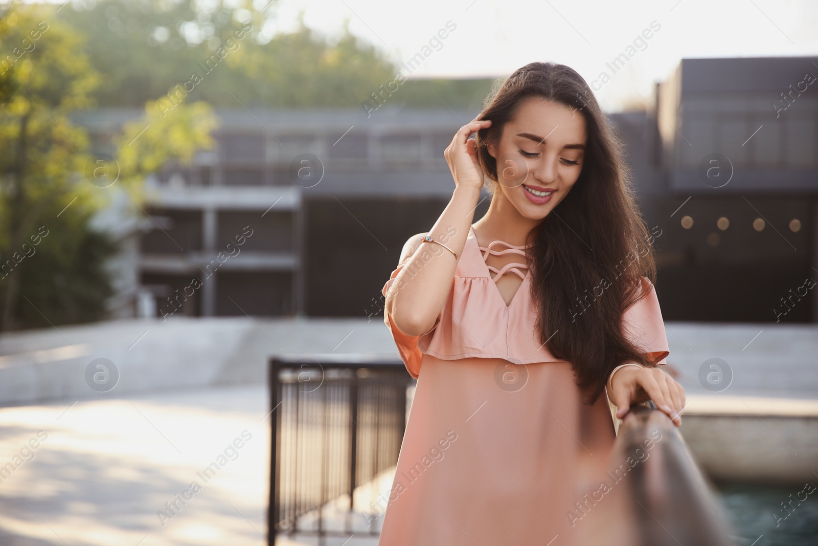 Photo of Beautiful young woman in stylish pink dress near railing outdoors