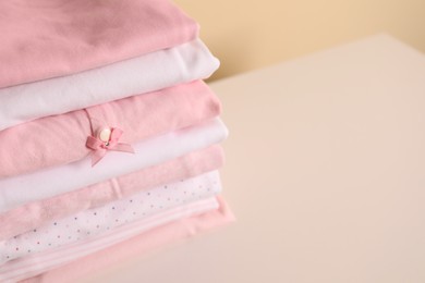 Photo of Stack of baby girl's clothes on white table, closeup. Space for text