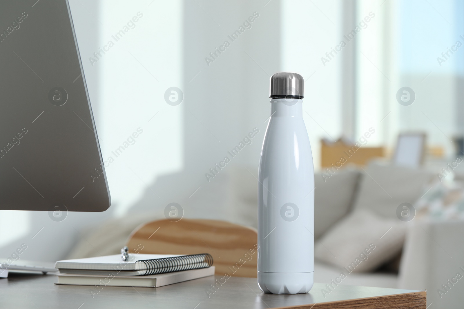 Photo of Stylish thermo bottle on wooden table at workplace in office