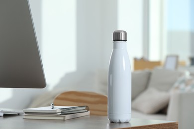 Photo of Stylish thermo bottle on wooden table at workplace in office