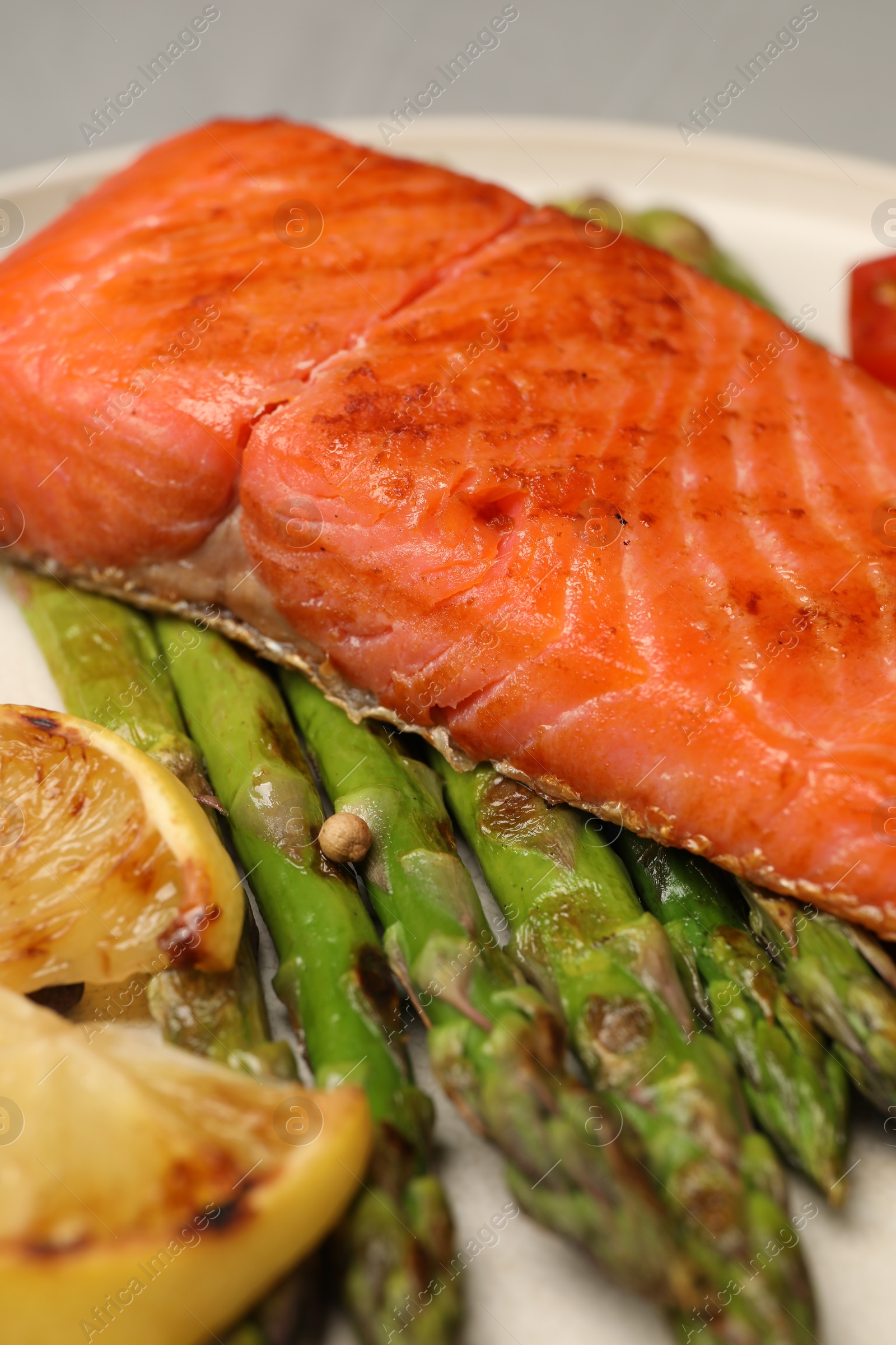 Photo of Tasty grilled salmon with asparagus, tomatoes and lemon on plate, closeup