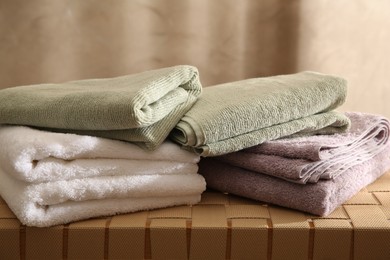 Photo of Stacks of soft towels on wicker bench indoors, closeup