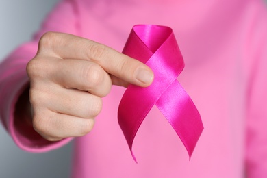 Woman holding pink ribbon on grey background, closeup. Breast cancer awareness