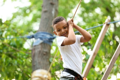 Photo of Little African-American boy climbing in adventure park. Summer camp