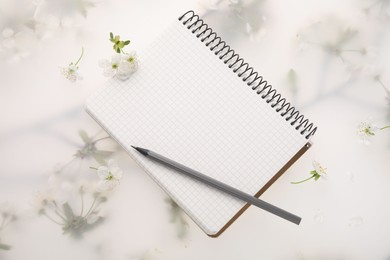 Photo of Guest list. Notebook, pencil and beautiful cherry tree blossoms on spring floral background, flat lay