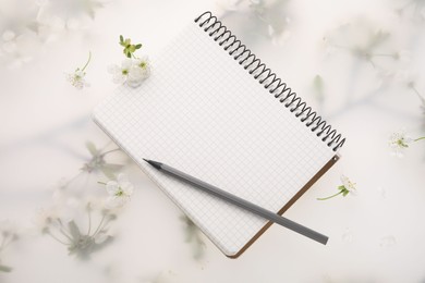 Guest list. Notebook, pencil and beautiful cherry tree blossoms on spring floral background, flat lay