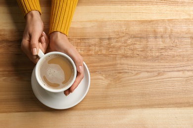 Photo of Woman holding cup of coffee at wooden table, top view. Space for text