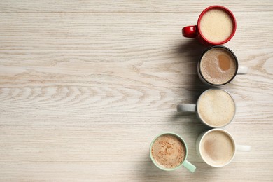 Photo of Many cups with different aromatic coffee on light wooden table, flat lay. Space for text
