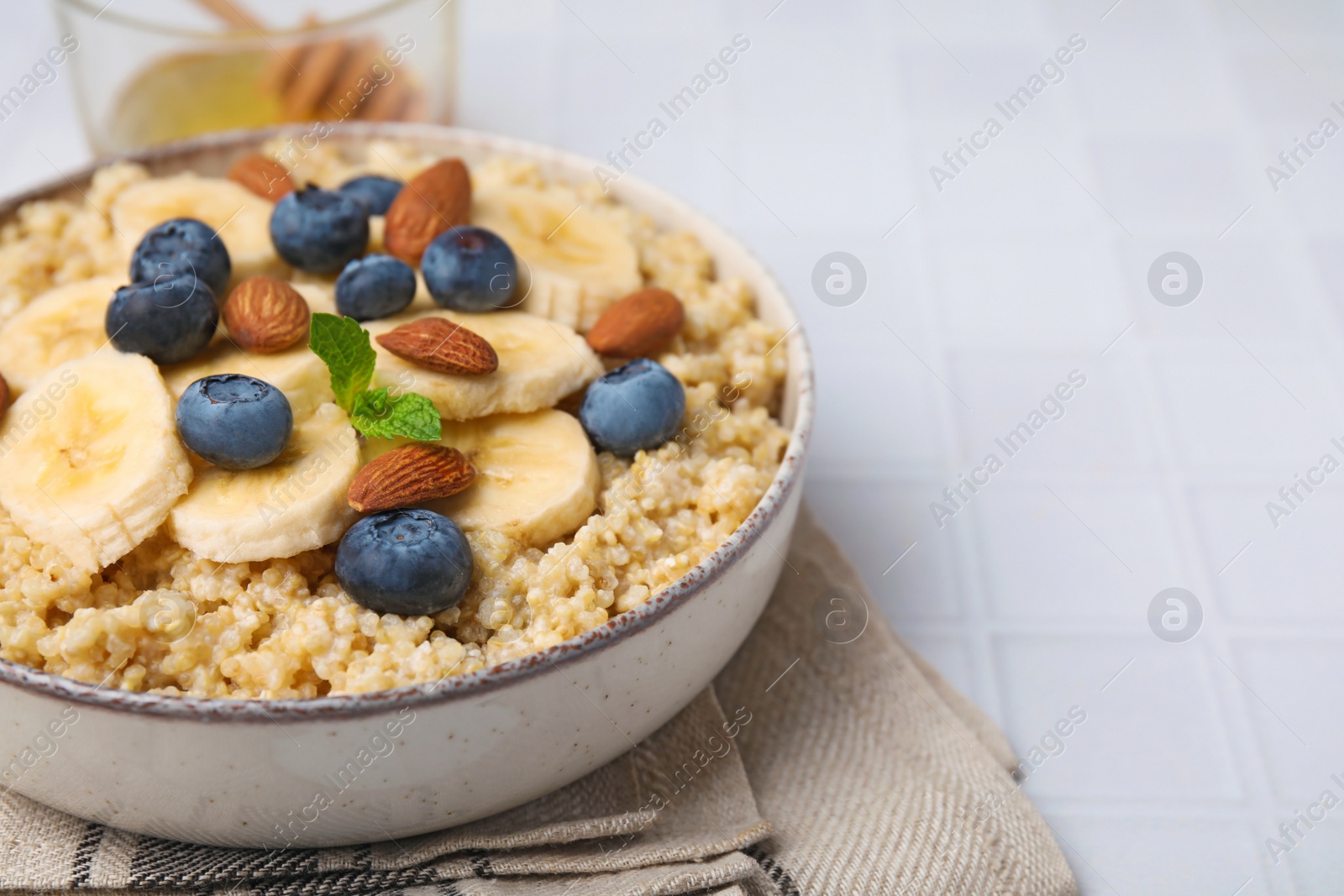 Photo of Bowl of delicious cooked quinoa with almonds, bananas and blueberries on white table, closeup. Space for text