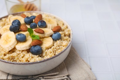 Bowl of delicious cooked quinoa with almonds, bananas and blueberries on white table, closeup. Space for text