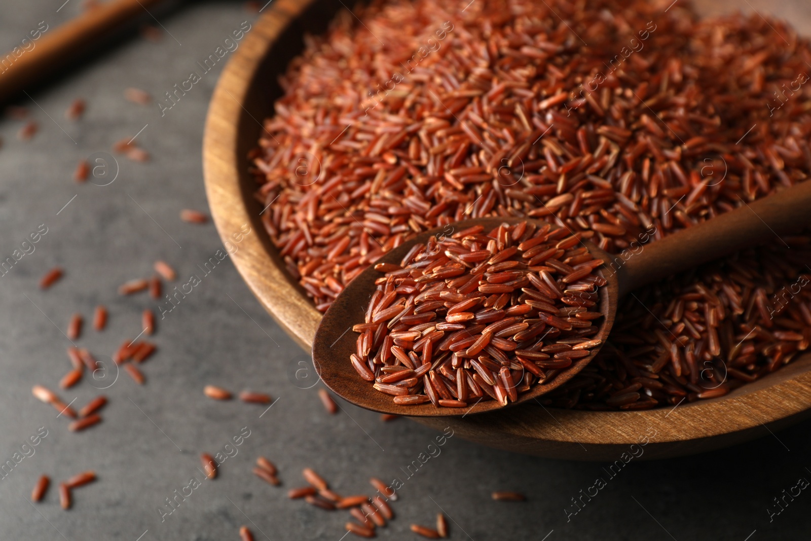 Photo of Closeup view of brown rice in spoon and bowl on table