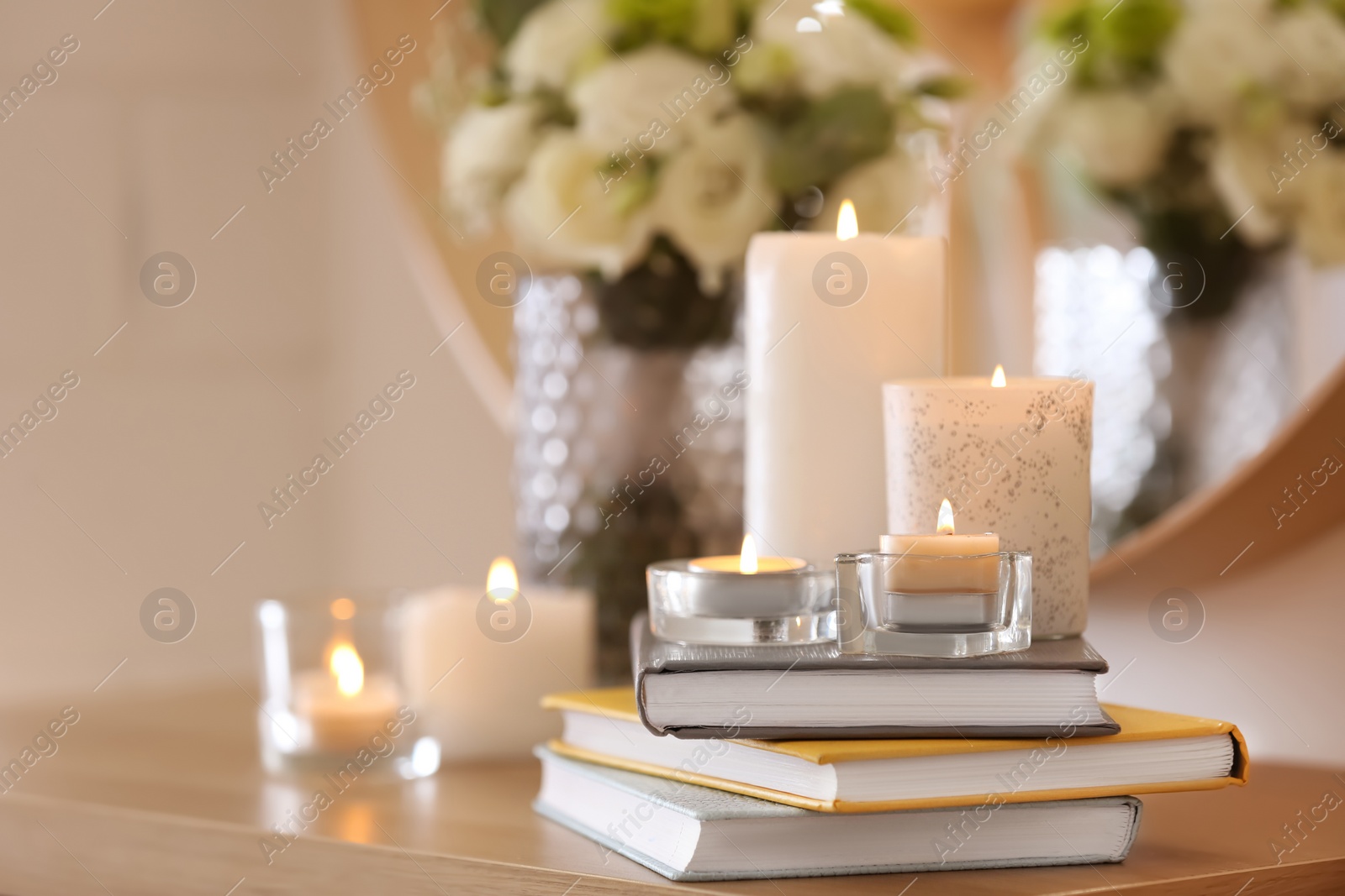 Photo of Beautiful burning candles, books and flowers on table at home