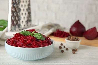 Photo of Bowl of grated boiled beets with basil and allspice on white wooden table