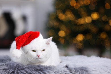 Photo of Adorable cat wearing Christmas hat on fur rug indoors. Space for text