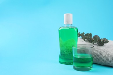 Fresh mouthwash in bottle, glass, towel and eucalyptus branch on light blue background. Space for text