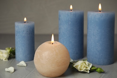 Burning candles and beautiful flowers on grey table