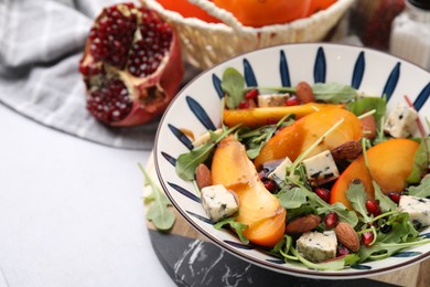 Photo of Tasty salad with persimmon, blue cheese, pomegranate and almonds served on white table, closeup. Space for text