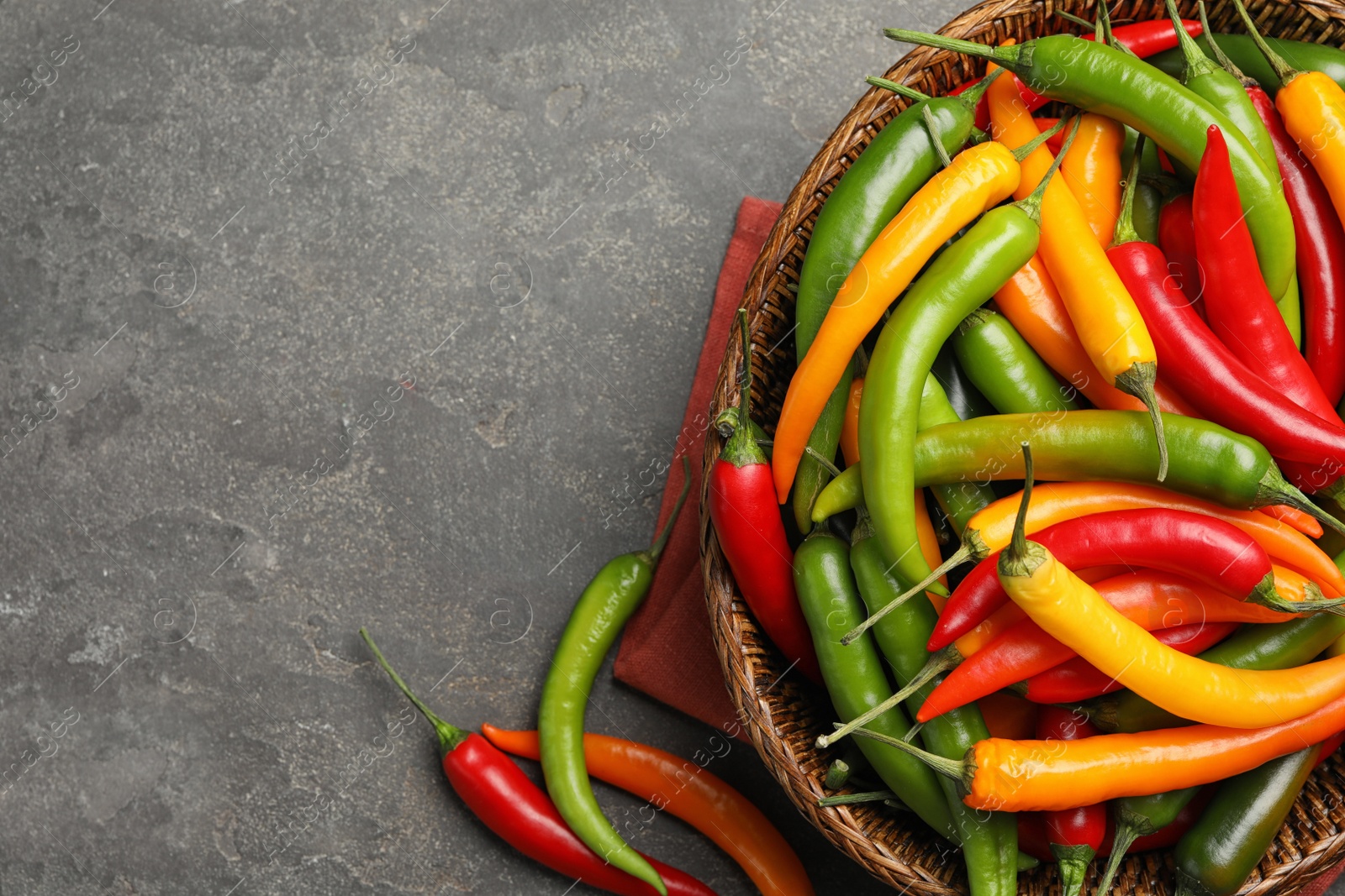 Photo of Wicker bowl with different chili peppers on grey table, flat lay. Space for text