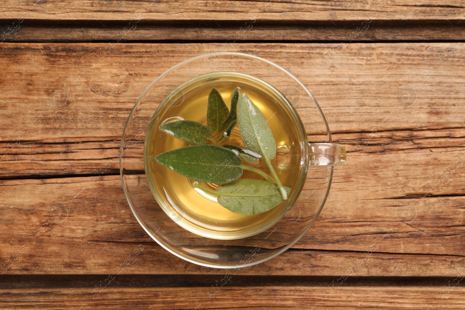 Photo of Cup of aromatic sage tea with fresh leaves on wooden table, top view