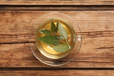 Photo of Cup of aromatic sage tea with fresh leaves on wooden table, top view