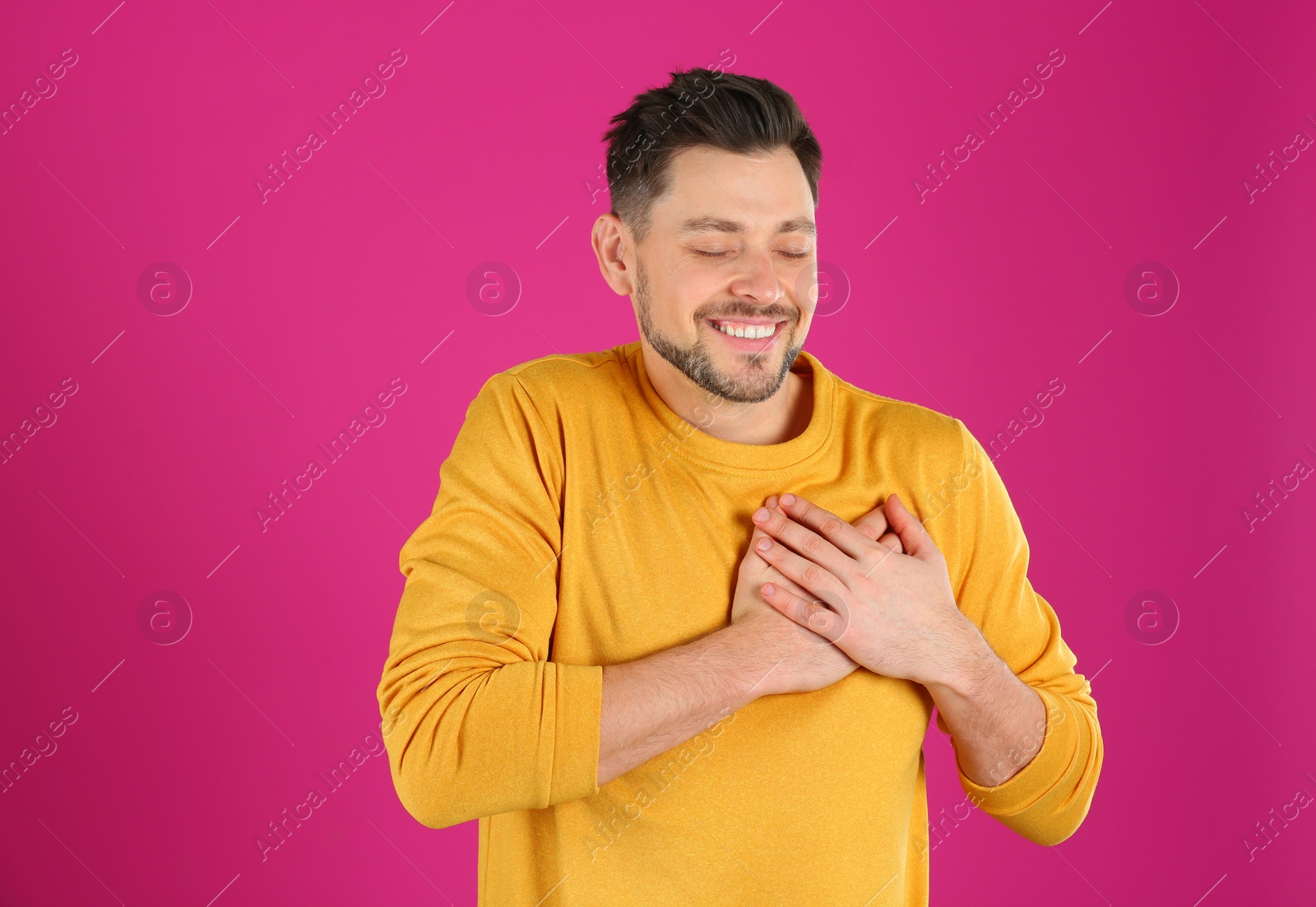 Photo of Portrait of handsome man holding hands near his heart on color background