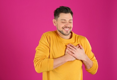 Portrait of handsome man holding hands near his heart on color background
