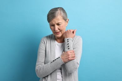 Photo of Arthritis symptoms. Woman suffering from pain in arm on light blue background