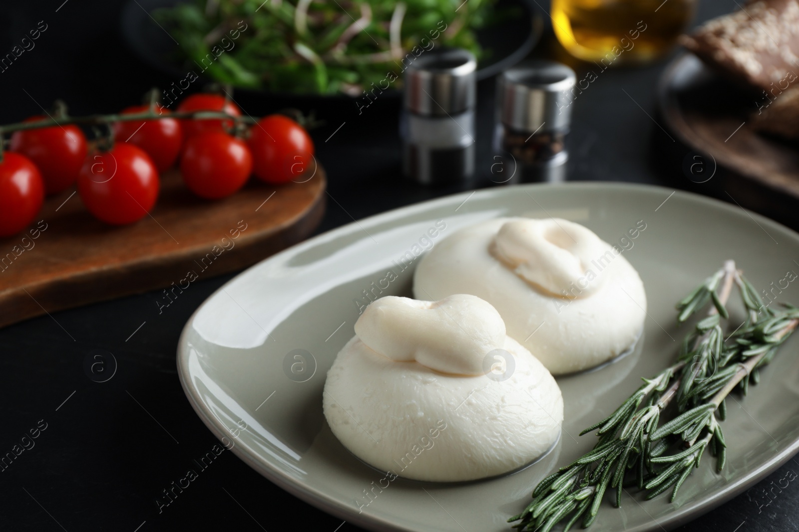 Photo of Delicious burrata cheese with rosemary on black table, closeup