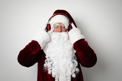 Photo of Santa Claus with headphones listening to Christmas music on light background