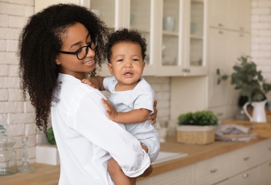 Photo of African-American woman with her baby in kitchen. Happiness of motherhood