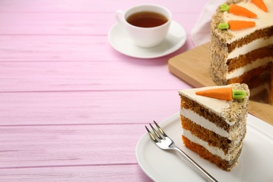 Photo of Sweet carrot cake with delicious cream on pink wooden table, space for text