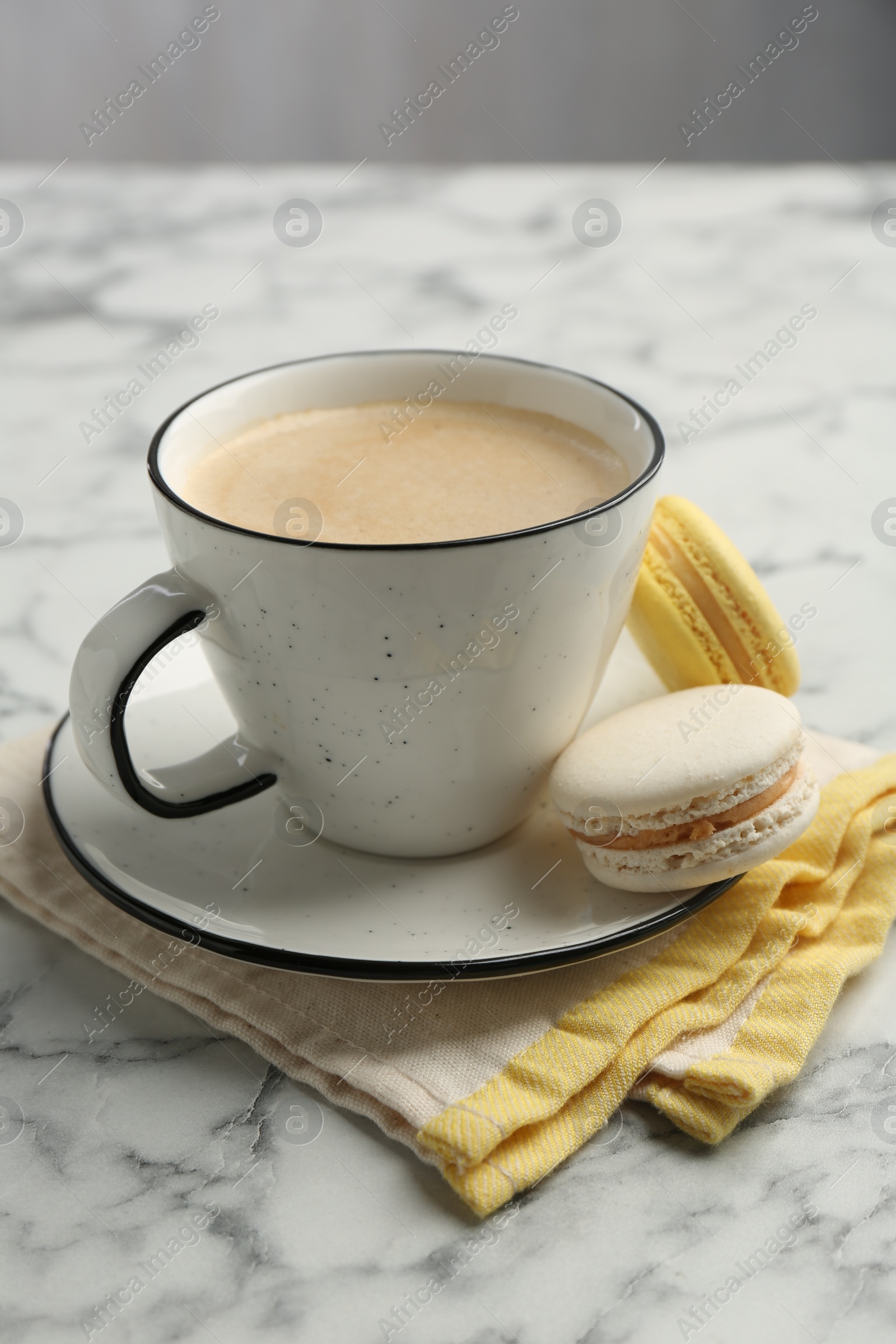 Photo of Tasty cappuccino in cup, macarons and saucer on white marble table, closeup