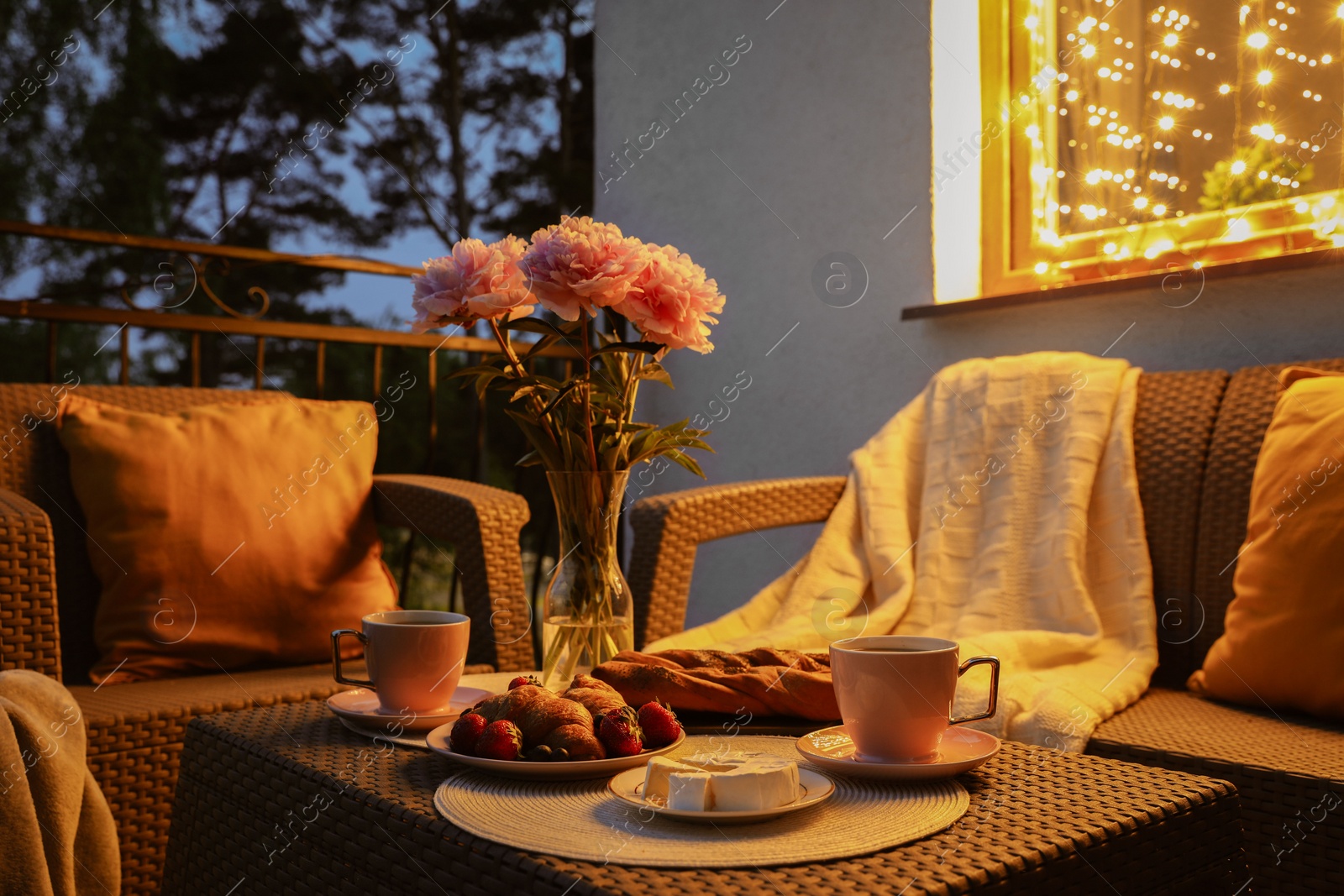 Photo of Rattan table with drink, food and flowers on outdoor terrace in evening