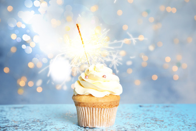 Delicious birthday cupcake with sparkler on blue table against blurred lights