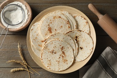 Many tasty homemade tortillas and rolling pin on wooden table, top view